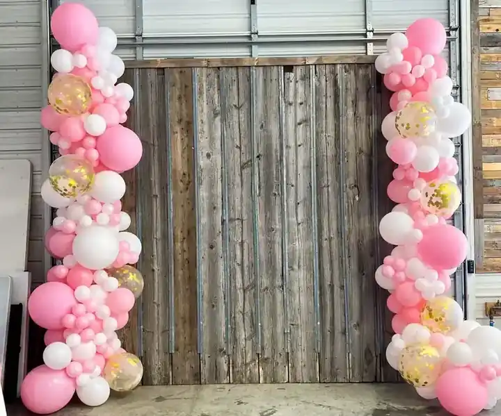 Pink and white balloon garland columns framing a barn-wood door
