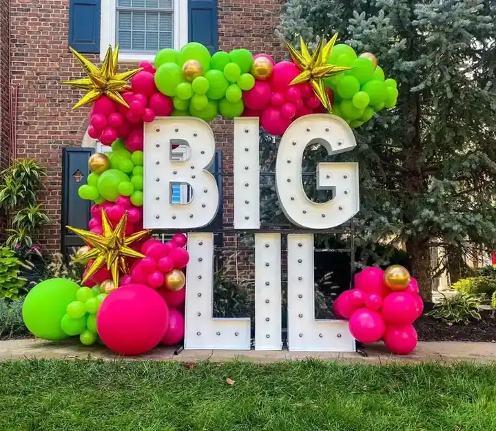 BIG LIL marquee letters wrapped in green, pink and gold balloons on a lawn