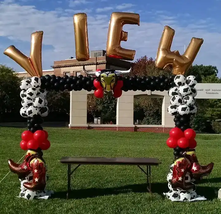 Cow-print and red balloon arch with gold foil letters on a lawn