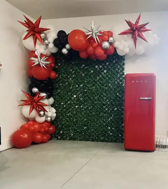 Red and white starburst balloon garland around a green hedge wall