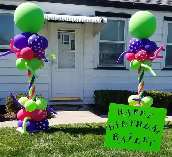 Two green and purple balloon columns beside a Happy Birthday yard sign